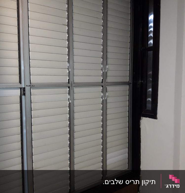 תריסים לבנים עם מסגרת מתכת בחלון פנימי